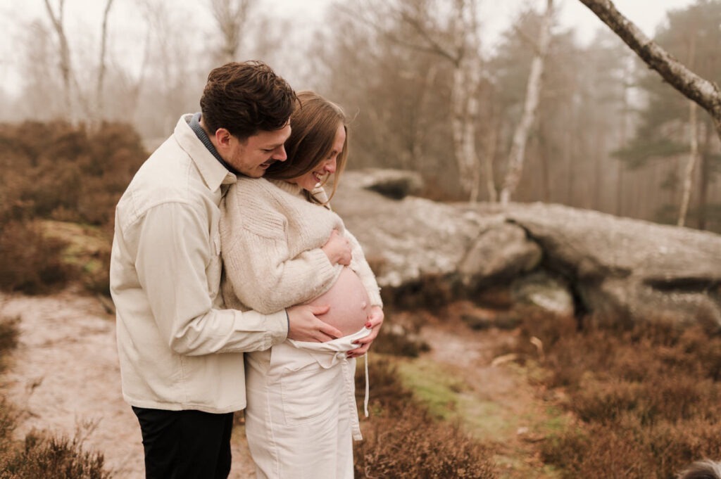 Mains sur le ventre et regards tendres pendant une séance photo grossesse en extérieur