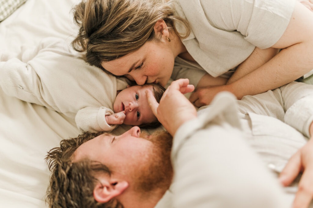 bébé allongé entre ses parents dans le lit, avec plein de tendresse lors d'une séance naissance à domicile dans l'Oise par Stéphanie Daillet photographe